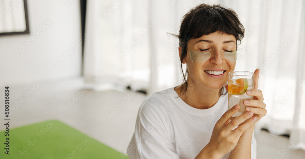 Tender young caucasian girl relaxing at home applying patches under eyes and refreshing water. Brunette with closed eyes wears white t-shirt. Medical cosmetic procedures concept Tender young caucasian girl relaxing at home applying patches under eyes and refreshing water. Brunette with closed eyes wears white t-shirt. Medical cosmetic procedures concept