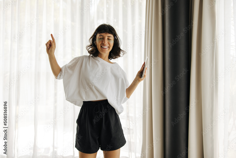 Cheerful young caucasian woman closing her eyes enjoys listening to music at home. Brunette wears white t-shirt and black shorts. Lifestyle concept Cheerful young caucasian woman closing her eyes enjoys listening to music at home. Brunette wears white t-shirt and black shorts. Lifestyle concept