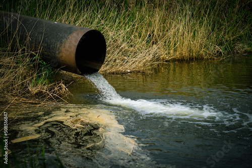 Draining sewage from pipe into river, pollution rivers and ecology.