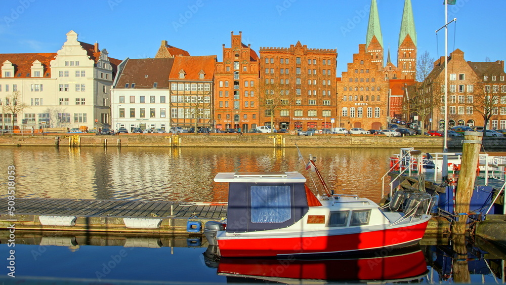 Naklejka premium historische Häuserfassaden und Kirchtürme in Lübeck entlang der Trave und rotes Boot im Vordergrund