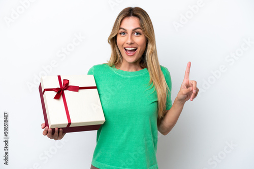 Young Uruguayan woman holding a gift isolated on white background pointing up a great idea