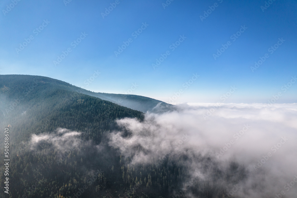 Aerial view of green mountains covered with clouds, clear blue sky. 