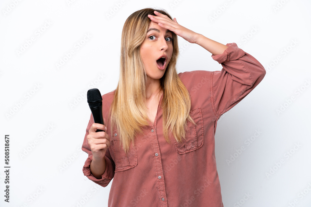 Singer Uruguayan woman picking up a microphone isolated on white background doing surprise gesture while looking to the side Singer Uruguayan woman picking up a microphone isolated on white background doing surprise gesture while looking to the side