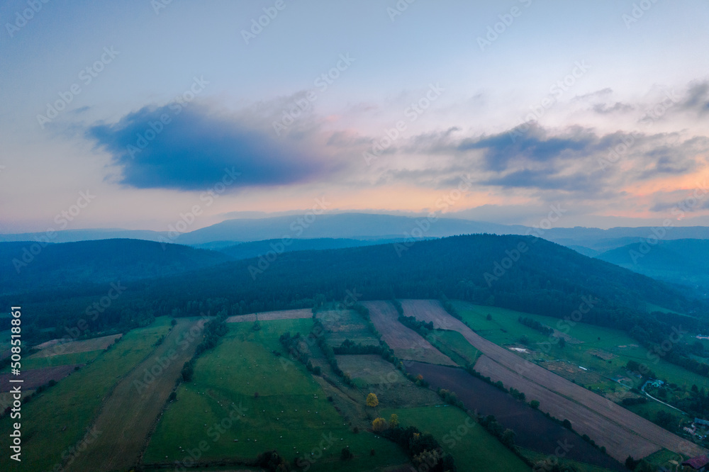 Sunrise over the green mountains and fields. Pastel colors in the sky.