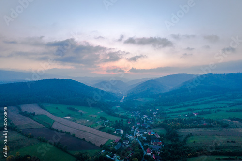 Sunrise over the green mountains and fields. Pastel colors in the sky, clouds over the peaks.