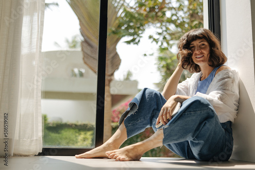 Fotobehang Pretty young caucasian woman looking at camera sitting by window in sunny weather