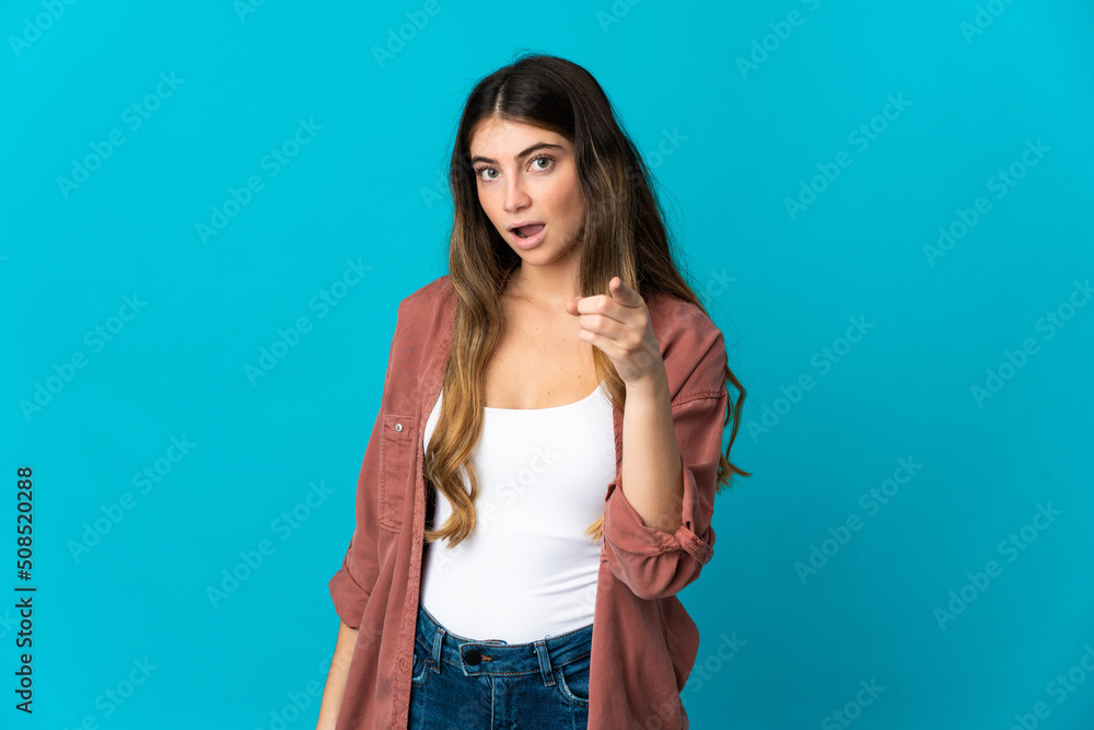 Young caucasian woman isolated on blue background surprised and pointing front Young caucasian woman isolated on blue background surprised and pointing front
