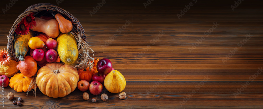 Thanksgiving day background with empty copy space. Pumpkin harvest in wicker basket. Squash, orange vegetable autumn fruit, apples, and nuts on a wooden table. Halloween decoration fall design - obrazy, fototapety, plakaty 