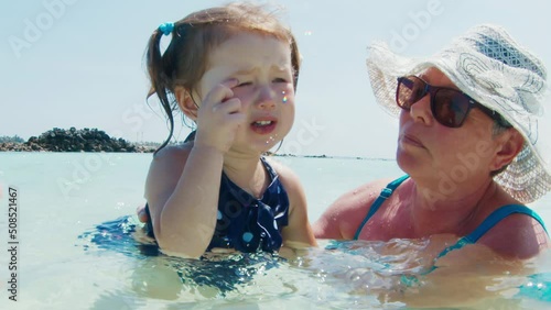 Salty water in the eyes. Toddler girls cries and rubs the eye irritated by sea water photo