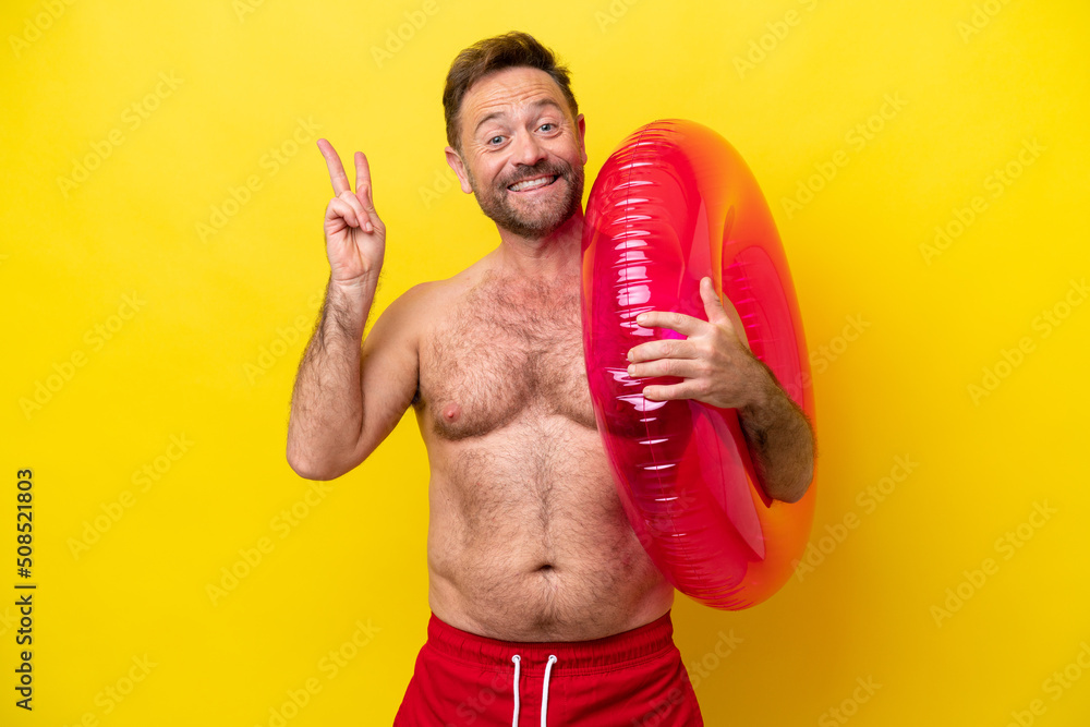 Middle age caucasian man holding inflatable donut isolated on yellow background smiling and showing victory sign