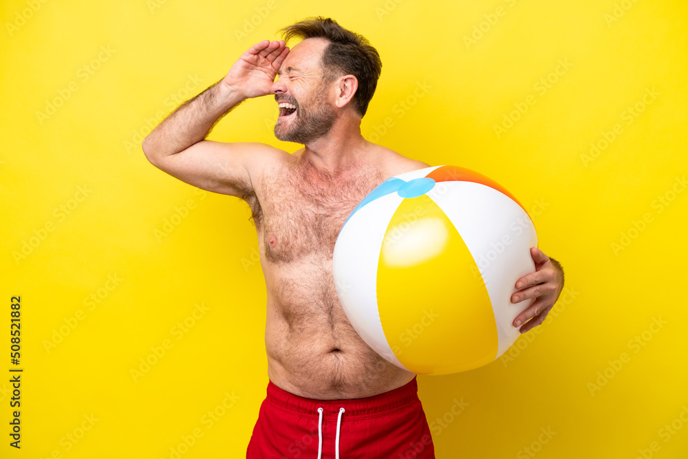 Middle age caucasian man holding beach ball isolated on yellow background smiling a lot Middle age caucasian man holding beach ball isolated on yellow background smiling a lot