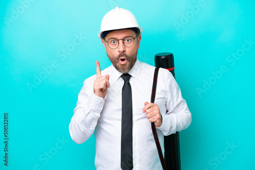 Middle age architect man with helmet and holding blueprints isolated on blue background intending to realizes the solution while lifting a finger up