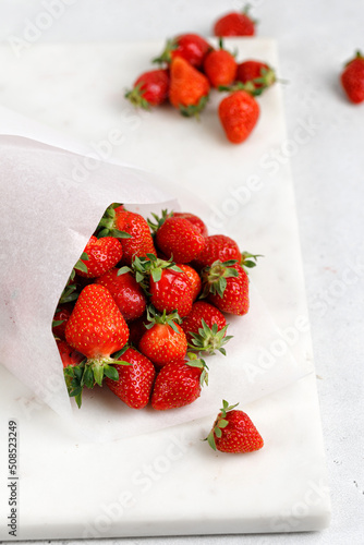 Fresh strawberries wrapped in a paper bag on marble board and grey background. Berry take away.