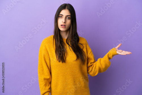 Young caucasian woman isolated on purple background making doubts gesture © luismolinero