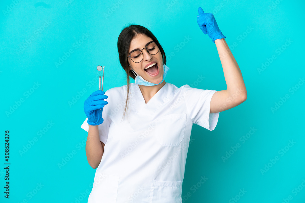 Young caucasian dentist woman holding tools isolated on blue background celebrating a victory Young caucasian dentist woman holding tools isolated on blue background celebrating a victory