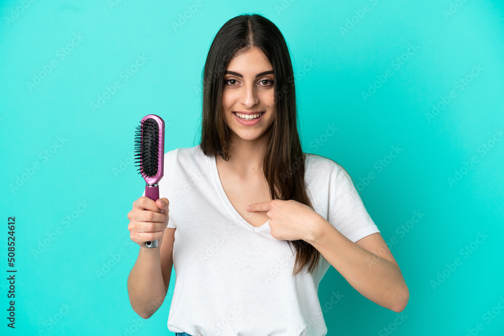 Young caucasian woman with hair comb isolated on blue background with surprise facial expression Young caucasian woman with hair comb isolated on blue background with surprise facial expression