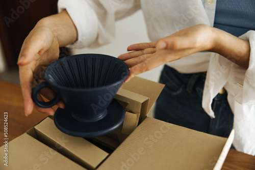 Close-up fair-skinned woman holding beautiful clay cup in her hands taking it out of box. Delivery concepts