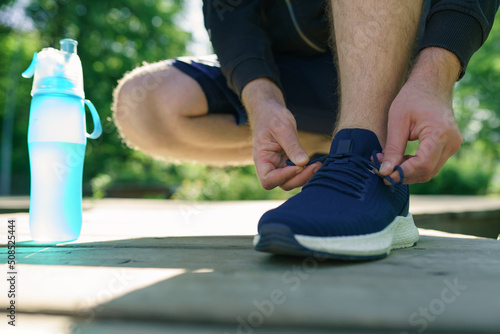 Man tying running shoes in the park outdoor, male runner ready for jogging on the road outside