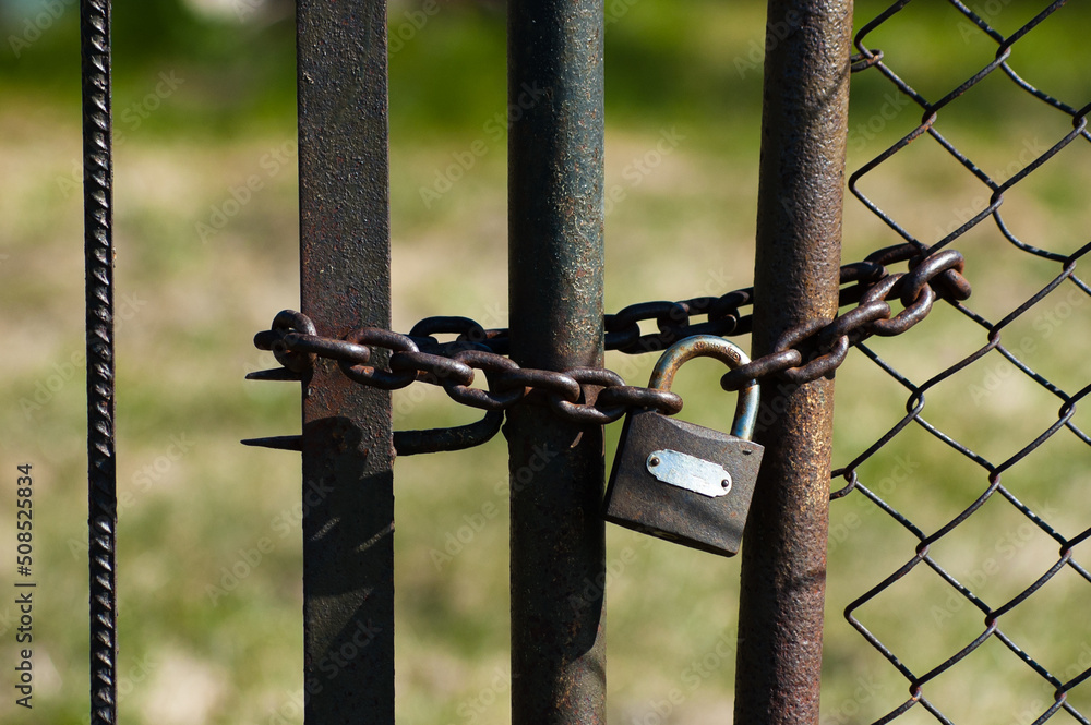 in the photo, a metal fence, a mesh chain and a lock in the photo, a metal fence, a mesh chain and a lock