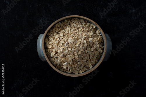 Top view of handmade ceramic bowl of organic oats on dark moody background.