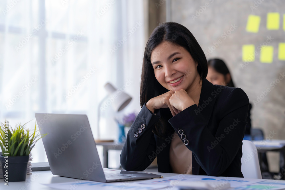 Charming young asian businesswoman sitting at her office desk and smiling to camera. Portrait of woman in office Charming young asian businesswoman sitting at her office desk and smiling to camera. Portrait of woman in office