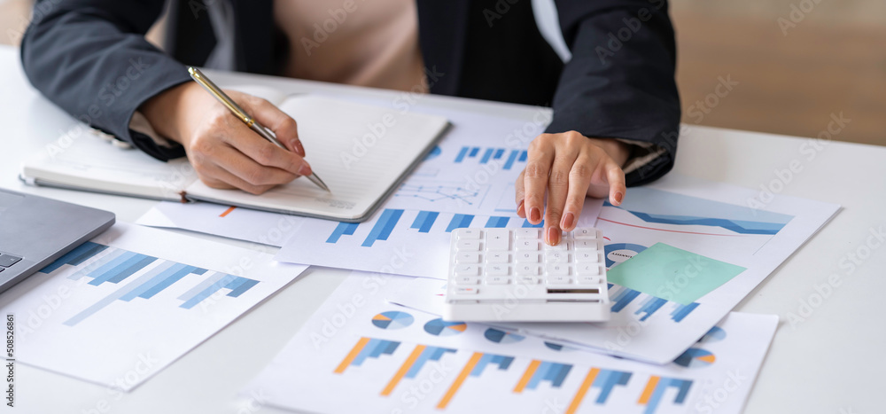Close up Business woman using calculator and laptop for do math finance on wooden desk in office and business working background, tax, accounting, statistics and analytic research concept Close up Business woman using calculator and laptop for do math finance on wooden desk in office and business working background, tax, accounting, statistics and analytic research concept