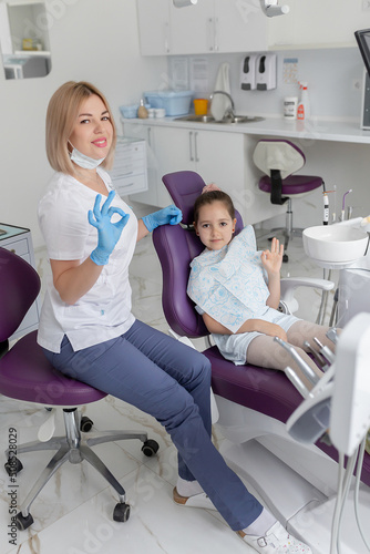 Dental clinic visit. Young positive woman dentist and small girl patient in dentist office
