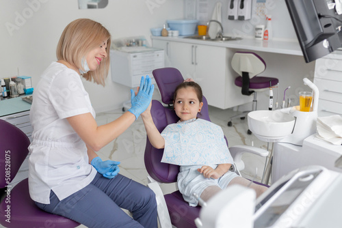 A child is happy after dental treatment and giving high-five to his doctor in a modern white dental clinic.