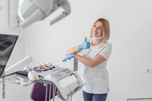 Young positive woman dentist showing thumbs up sign in dentist office