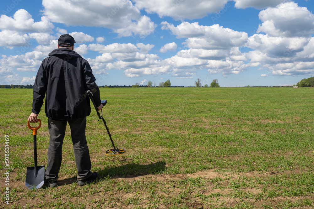 Treasure hunter. Man with metal detector. Human search treasure on green  field. Guy with metal detector and shovel. Treasure hunter with his back to  camera. Concept of archaeological excavations Stock Photo