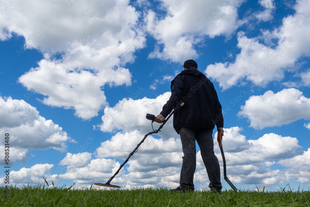Foto Stock Archaeologist with metal detector. Man with shovel surveys lawn.  Guy on background of sky. Archaeologist with device for searching for metal.  Metal detector to search for treasure in person hand