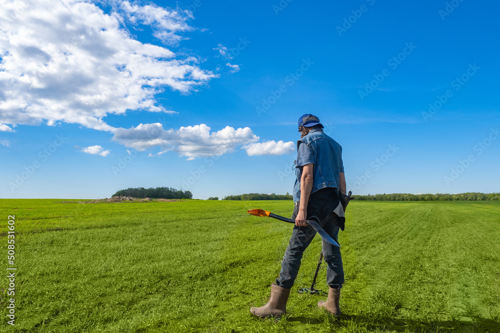 Treasure seeker man. Guy with metal detector with his back to camera. Treasure hunter holds shovel and metal sensor. Search for golden treasure concept. Man with metal detector under blue sky