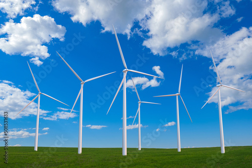 Windmill farm. Panorama with wind energy generators. Green meadow with windmills. White wind turbines. Windmills are spinning on summer day. Green energy generators. Renewable energy.