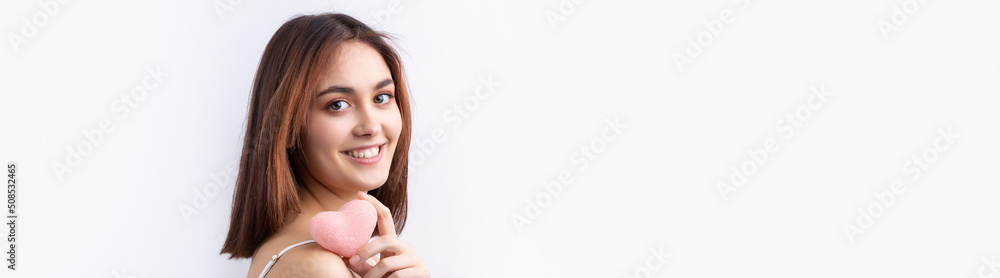 Beautiful smiling woman with clean skin, natural make-up and white teeth on a gray background. Holding a pink hygienic heart. Beautiful smiling woman with clean skin, natural make-up and white teeth on a gray background. Holding a pink hygienic heart.