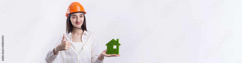 A young girl architect in a construction helmet demonstrates a model of a green house. Sale of ecological real estate. A young girl architect in a construction helmet demonstrates a model of a green house. Sale of ecological real estate.