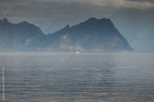 sailing yacht is on the horizon, norwegian seascape, rocky coast with dramatic skies, the sun breaks through the clouds, sheer cliffs, small islands illuminated by the sun