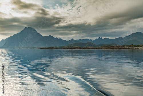 Norwegian seascape, lighthouse on the island, rocky coast with dramatic skies, the sun breaks through the clouds, sheer cliffs, small islands illuminated by the sun © Vladimir Drozdin