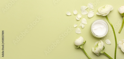 Jar of cosmetic cream and beautiful flowers on green background with space for text