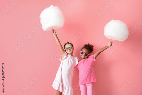 Cute little girls with cotton candy on pink background photo
