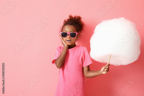 Little African-American girl with cotton candy on pink background photo