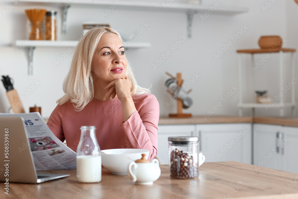Morning of mature woman reading newspaper in kitchen Morning of mature woman reading newspaper in kitchen