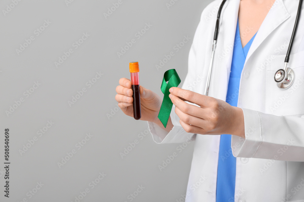 Female doctor with green ribbon and blood sample on grey background. Liver cancer concept Female doctor with green ribbon and blood sample on grey background. Liver cancer concept