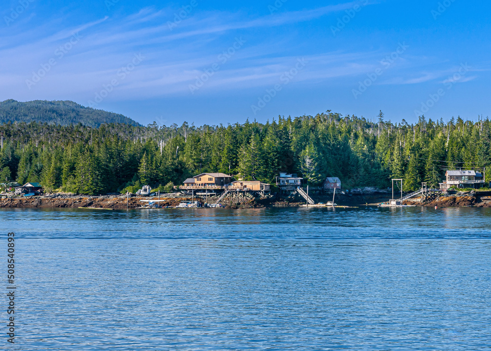 Ketchikan, Alaska, USA - July 17, 2011: Blue sky and blue water separated by green forested belt with a few buildings along shoreline. Ketchikan, Alaska, USA - July 17, 2011: Blue sky and blue water separated by green forested belt with a few buildings along shoreline.