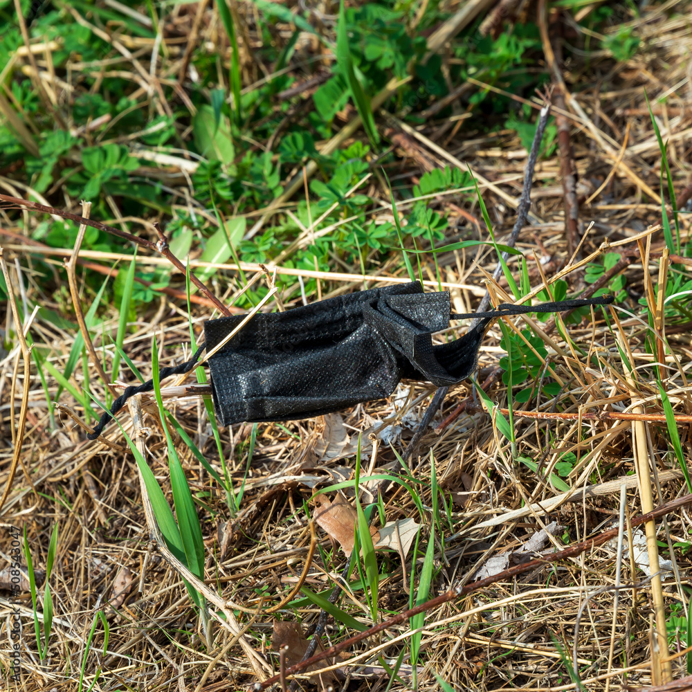 A discarded face mask lays tangled in springtime grass. A discarded face mask lays tangled in springtime grass.