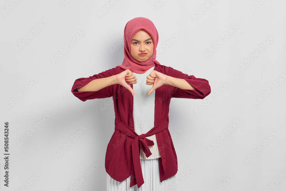 Disappointed beautiful Asian woman in casual shirt showing thumbs down, doing disapproval gesture isolated over white background