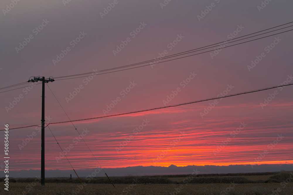 Electric power cables silhouetted against bright red sunset sky