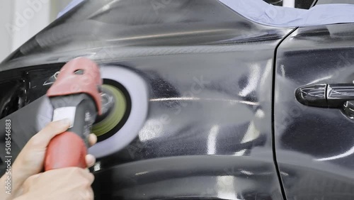 Worker polishing vehicle body with special grinder and wax from scratches at the car service station. Professional car detailing and maintenance concept.