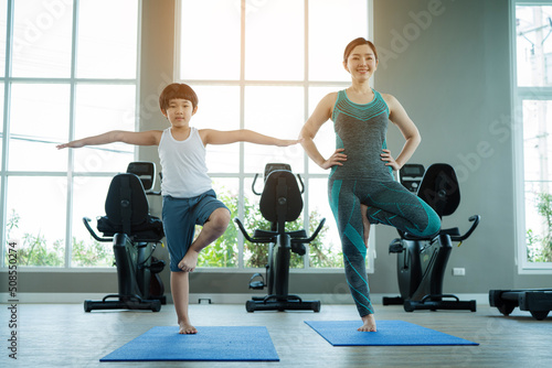 Mother with a little son having fun together and doing sport yoga in the fitness room. Mum playing with son.