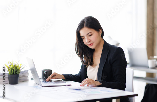 Happy attractive Asian businesswoman working with a laptop and financial document at the office, successful action, Business Finance, Technology concept.