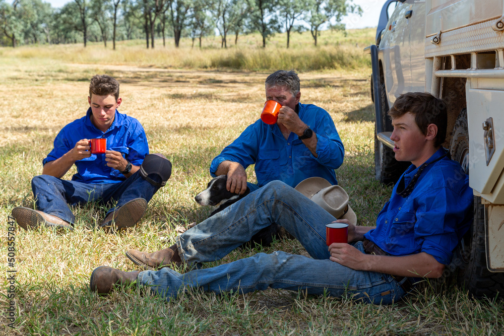Three males sitting on ground next to ute having morning tea smoko. Three males sitting on ground next to ute having morning tea smoko.